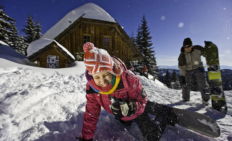 Spaß im Schnee mit dem Snowboard vor der Almhütte